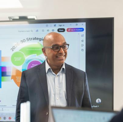 A man stands in an office, pitching an idea to colleagues who are listening.