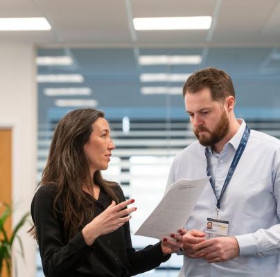 A close-up of a woman discussing information on paper with a man in an open office space.