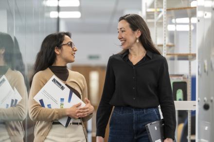 Two women having a discussion while walking through the office