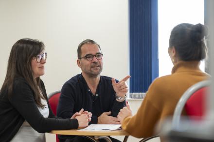 A man and two women sit together in a meeting, engaged in discussion