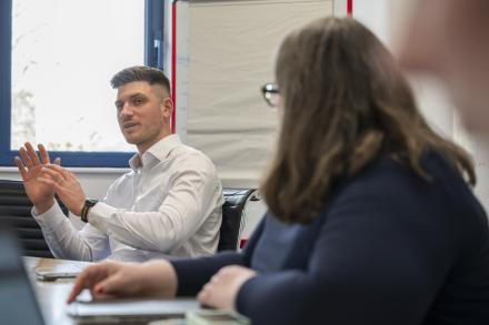 A man pitches an idea to colleagues who are listening in a room