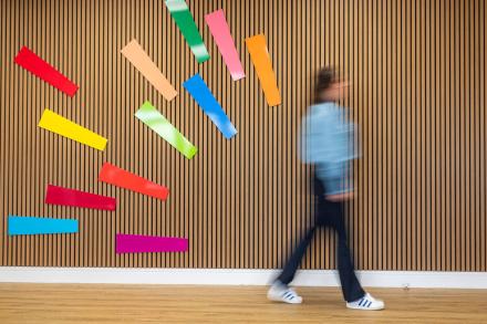 Blurred woman walking past a wall of vertical wooden slats decorated with the OUI sparks icon