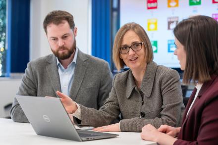 A male and two women are having a discussion together with a laptop open