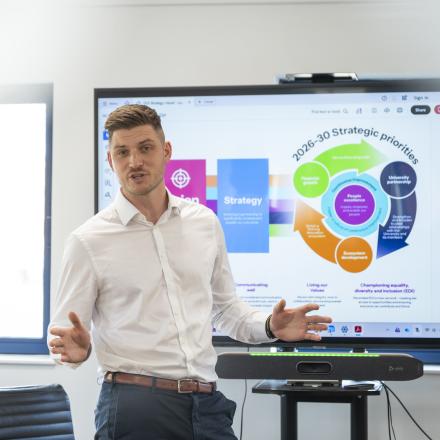 A man stands at the front of a room pitching to a diverse group of people
