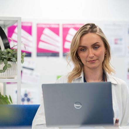 A close-up of a woman using her laptop while working in an open-plan office.