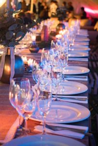 Formal dinner setting at a long table with white plates, wine glasses and centre pieces